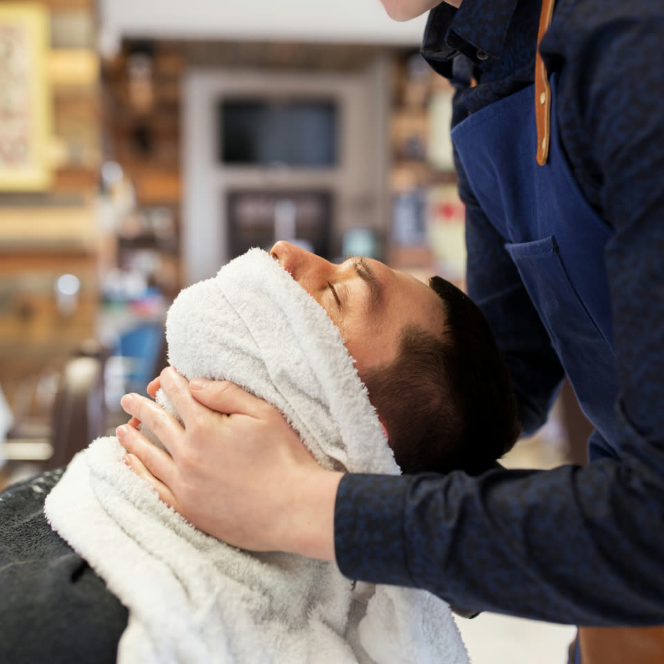 A hot towel laid over a client's face before a straight-razor shave